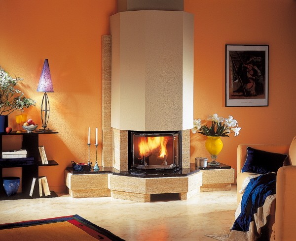 Narożny, obudowany piaskowcem, nowoczesny kominek z paleniskiem, płomienie widoczne przez szybę, pomarańczowe ściany w tle, minimalistyczne dekoracje.